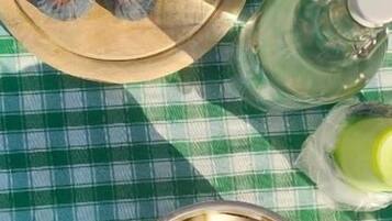 Una mesa con mantel a cuadros, un plato de madera con alimentos, un bol de metal con cubos y una botella de líquido.