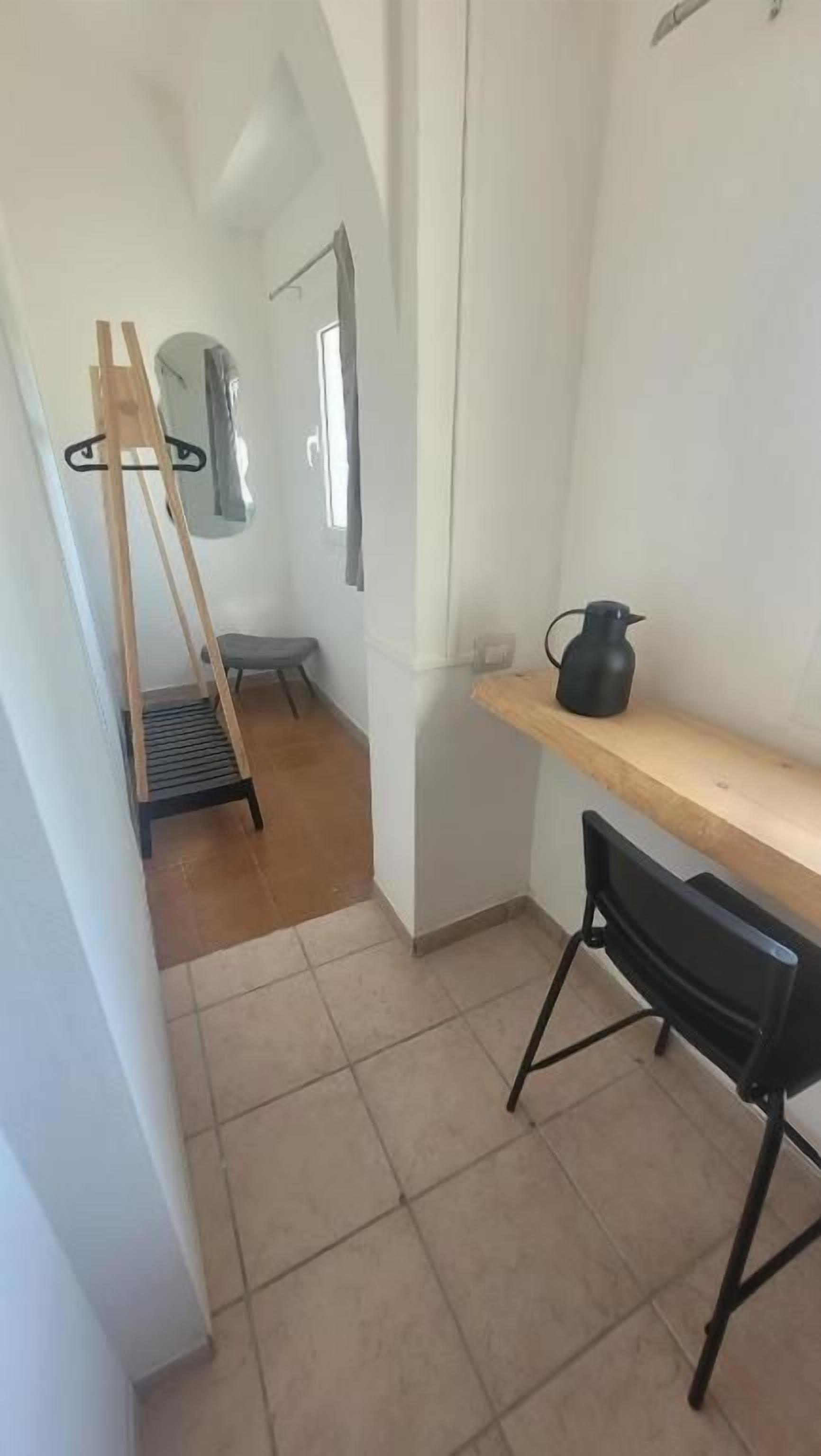 Een smalle gang met een houten ladder, een zwarte stoel en een houten plank met een zwarte kan.