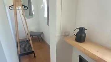 Un pasillo estrecho con una escalera de madera, una silla negra y un estante de madera con una jarra negra.