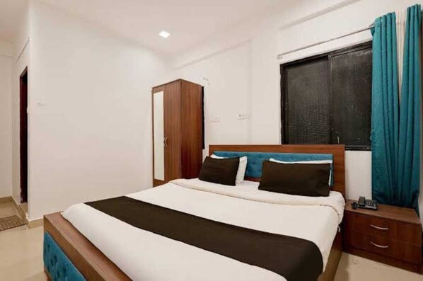 Habitació d'hotel amb llit, armari, tauleta de nit i finestra amb cortines.