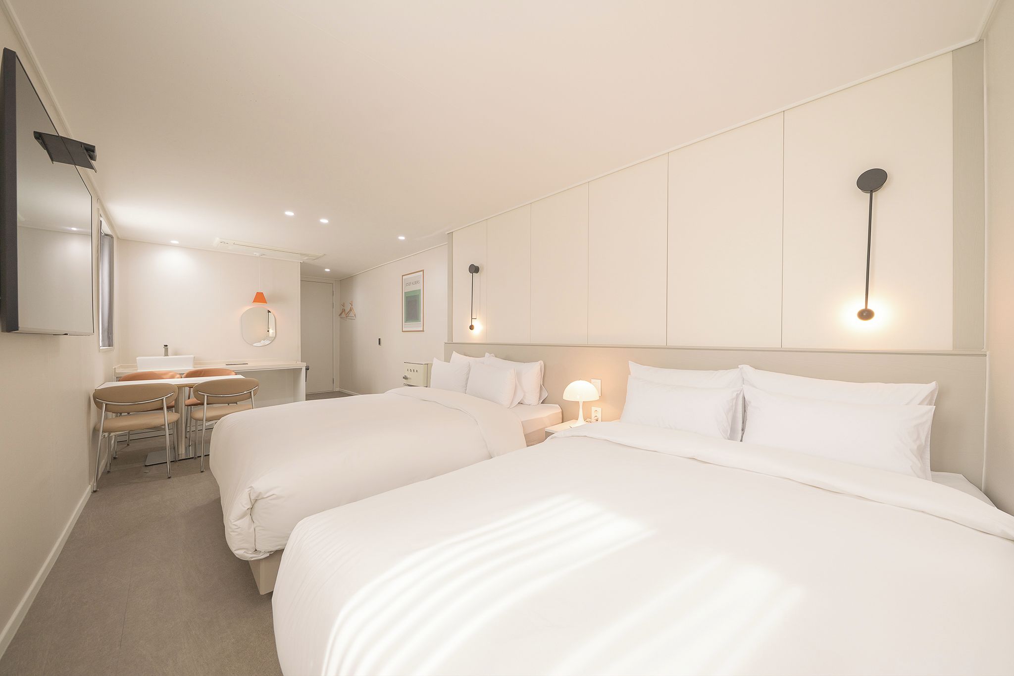 A hotel room with two beds, a desk, a chair, and a mirror.