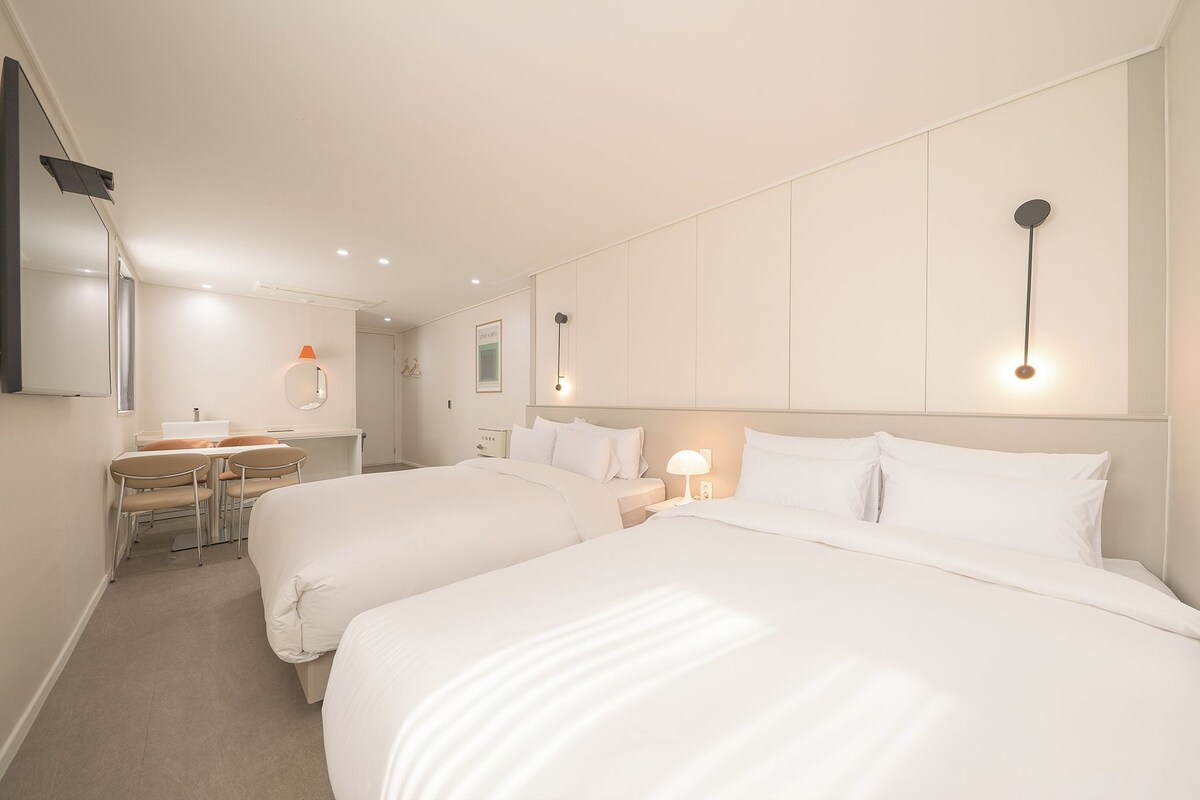 Hotellihuone, jossa on kaksi sänkyä, työpöytä, tuoli ja peili.