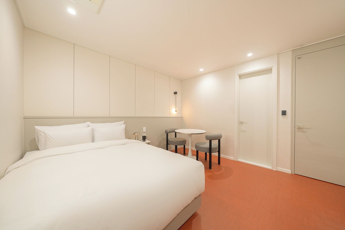 Hotellihuone, jossa on suuri sänky, pieni pyöreä pöytä, kaksi tuolia, yöpöytä ja vaatekaappi.
