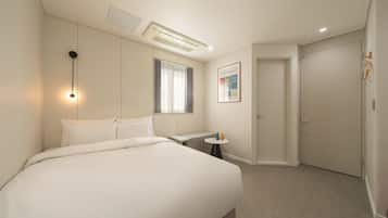 Une chambre d’hôtel avec un grand lit, une table de chevet, une petite table ronde, une fenêtre avec des rideaux, une porte et un climatiseur fixé au mur.