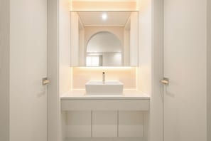 Un baño con lavamanos, espejo y armario blancos.