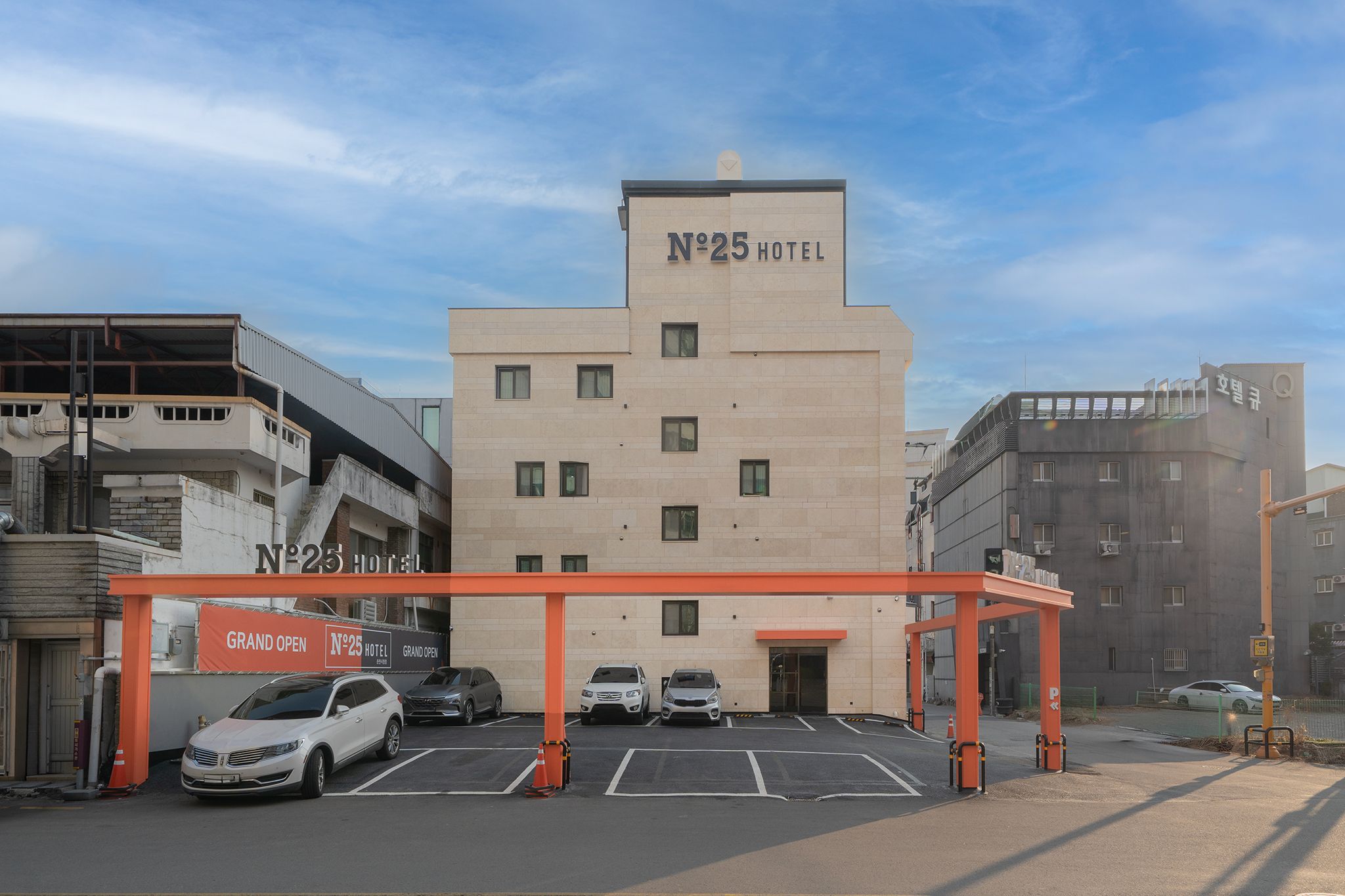 A hotel with a sign reading 'N°25 HOTEL' and a covered parking area with several cars.