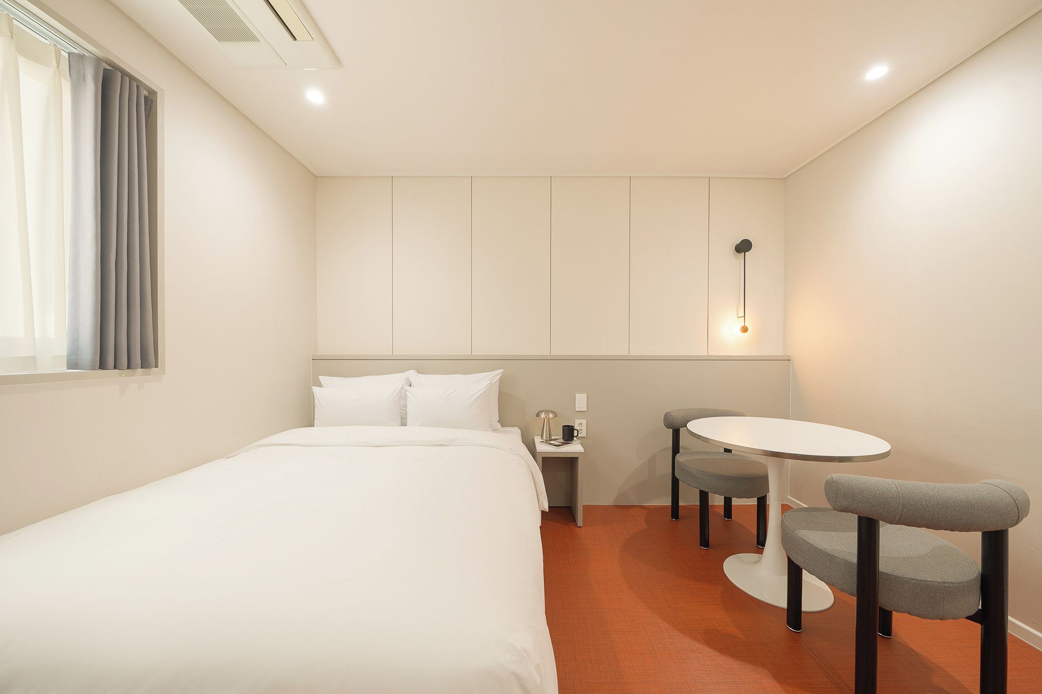A hotel room with a bed, a small table with two chairs, a nightstand, and a wall-mounted light fixture.