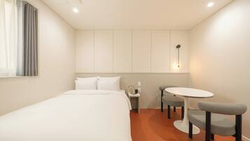 A hotel room with a bed, a small table with two chairs, a nightstand, and a wall-mounted light fixture.