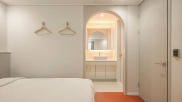 Quarto de hotel com cama, banheiro com pia e espelho, e porta com leitor de cartão.