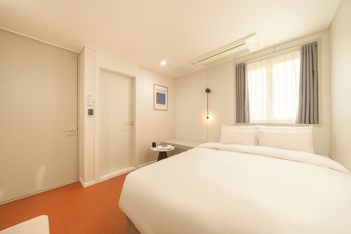 A hotel room with a bed, bedside table, and a window with curtains.