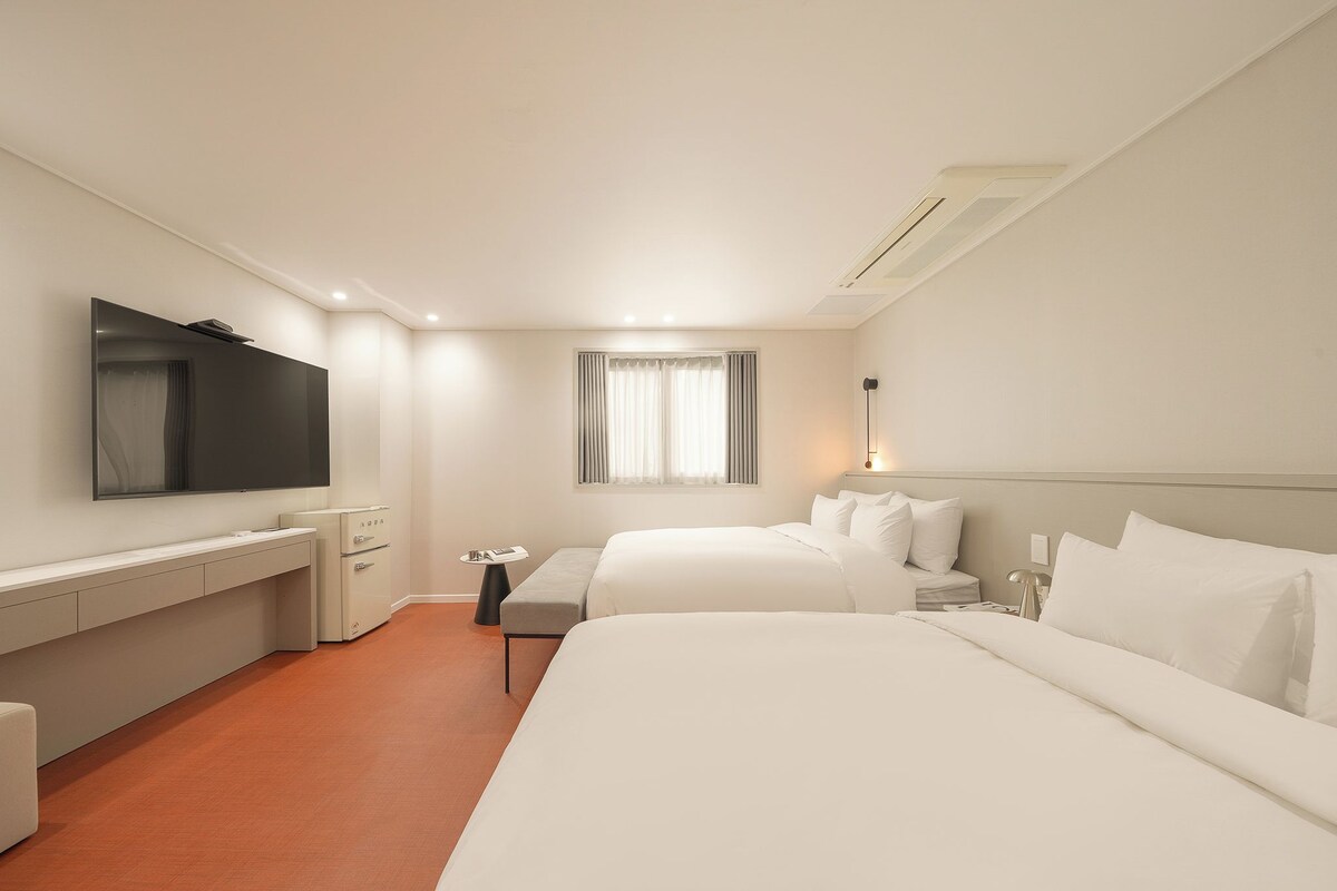 Hotellihuone, jossa on sänky, työpöytä, televisio ja ikkuna, jossa on verhot.