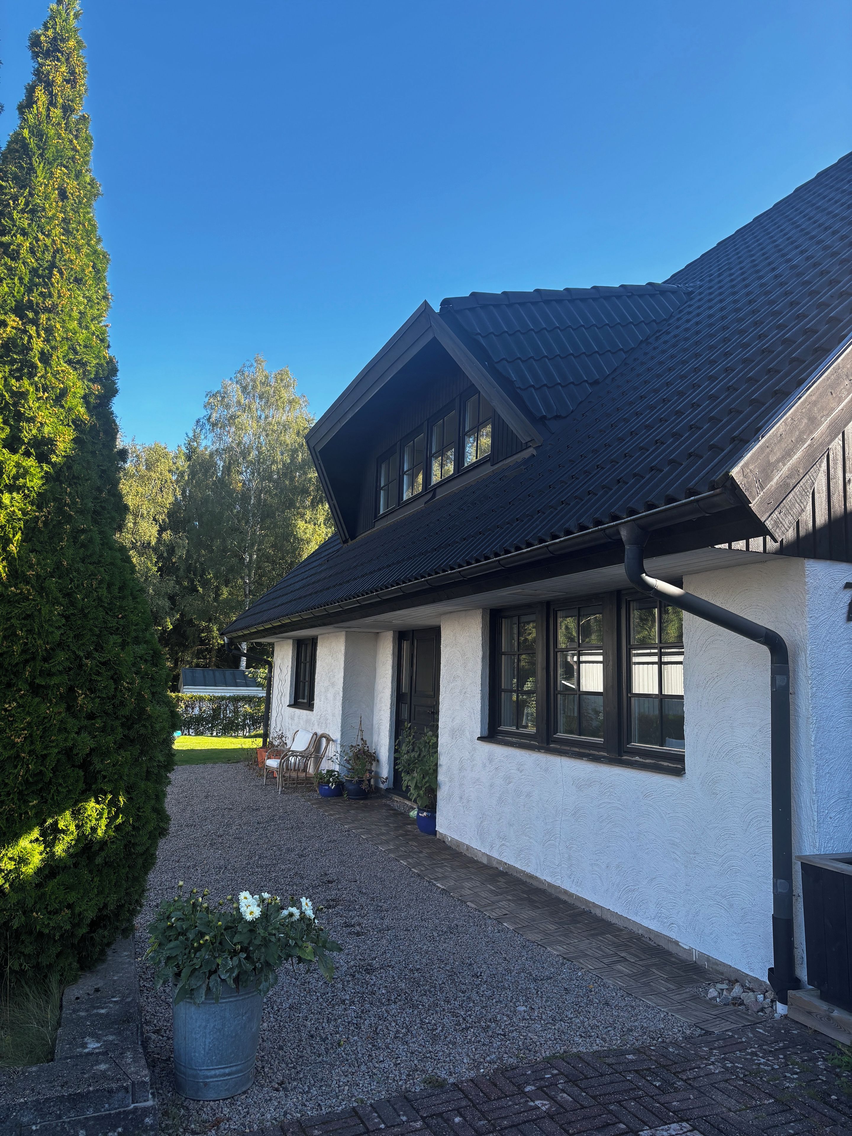 Ett hus med ett sluttande tak, en grusuppfart och ett stort träd till vänster.