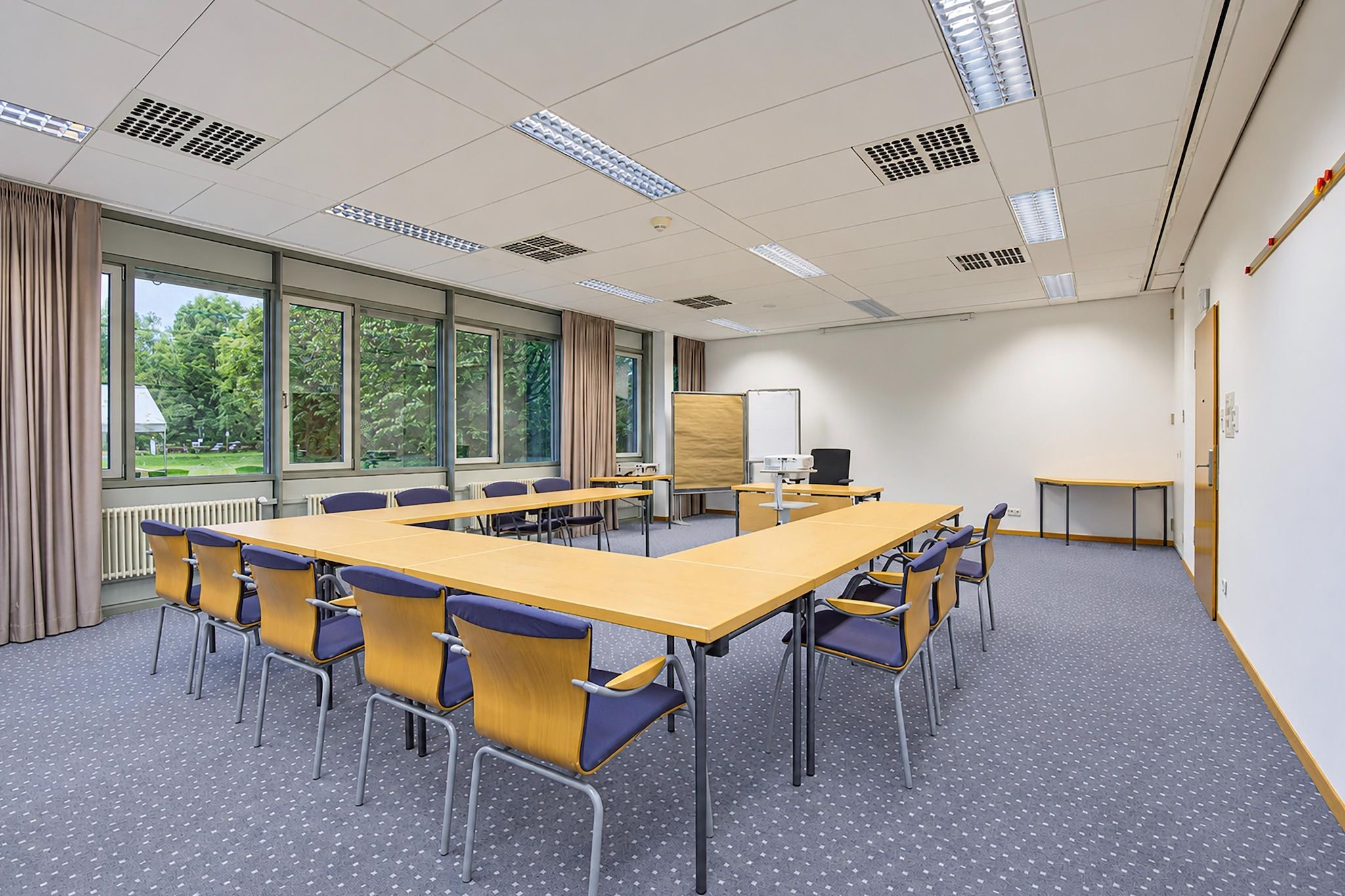 Ein Konferenzraum mit einem langen Tisch, Stühlen, einer Whiteboard-Tafel und großen Fenstern.
