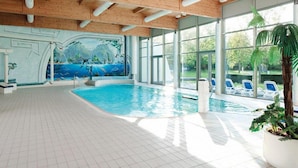 Una piscina interior con un mural, vigas de madera en el techo y vistas al exterior.