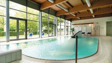 Ein Innenpool mit großen Glaswänden, einer Holzbalkendecke und einem gefliesten Boden.