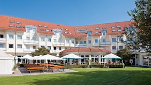Un hotel de varios pisos con techo de tejas rojas, un área de estar al aire libre con mesas y sillas, y un césped bien cuidado.
