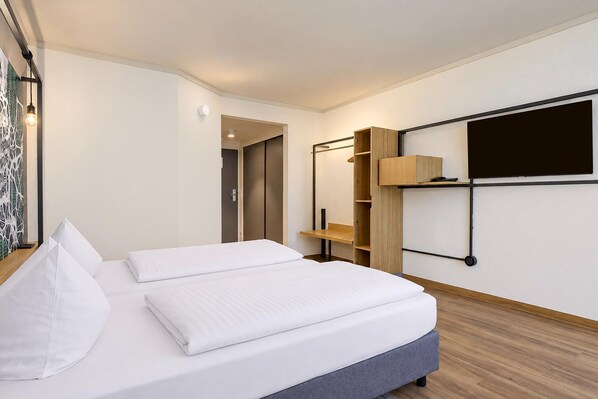 A modern hotel room with a bed, a wardrobe, a desk, and a mounted TV.