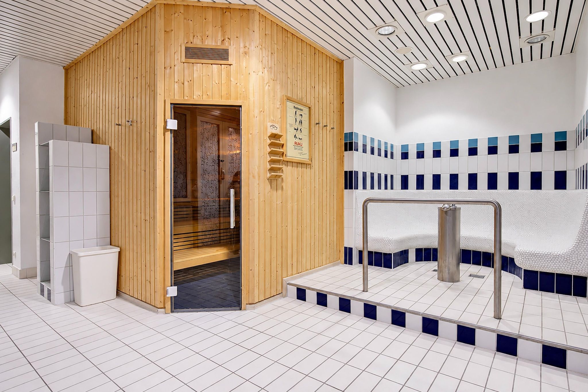 Et sauna rum med en trædør, flisegulv og en flisevæg i blå og hvid.