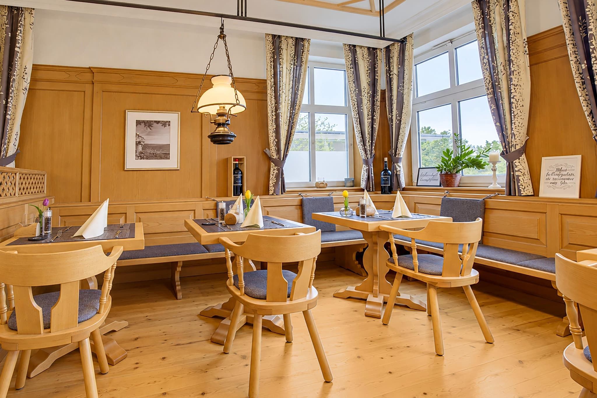 Ein Hotelzimmer mit Holzvertäfelung, einem Essbereich mit Holztischen und -stühlen sowie großen Fenstern mit Vorhängen.