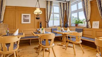 Ein Hotelzimmer mit Holzvertäfelung, einem Essbereich mit Holztischen und -stühlen sowie großen Fenstern mit Vorhängen.