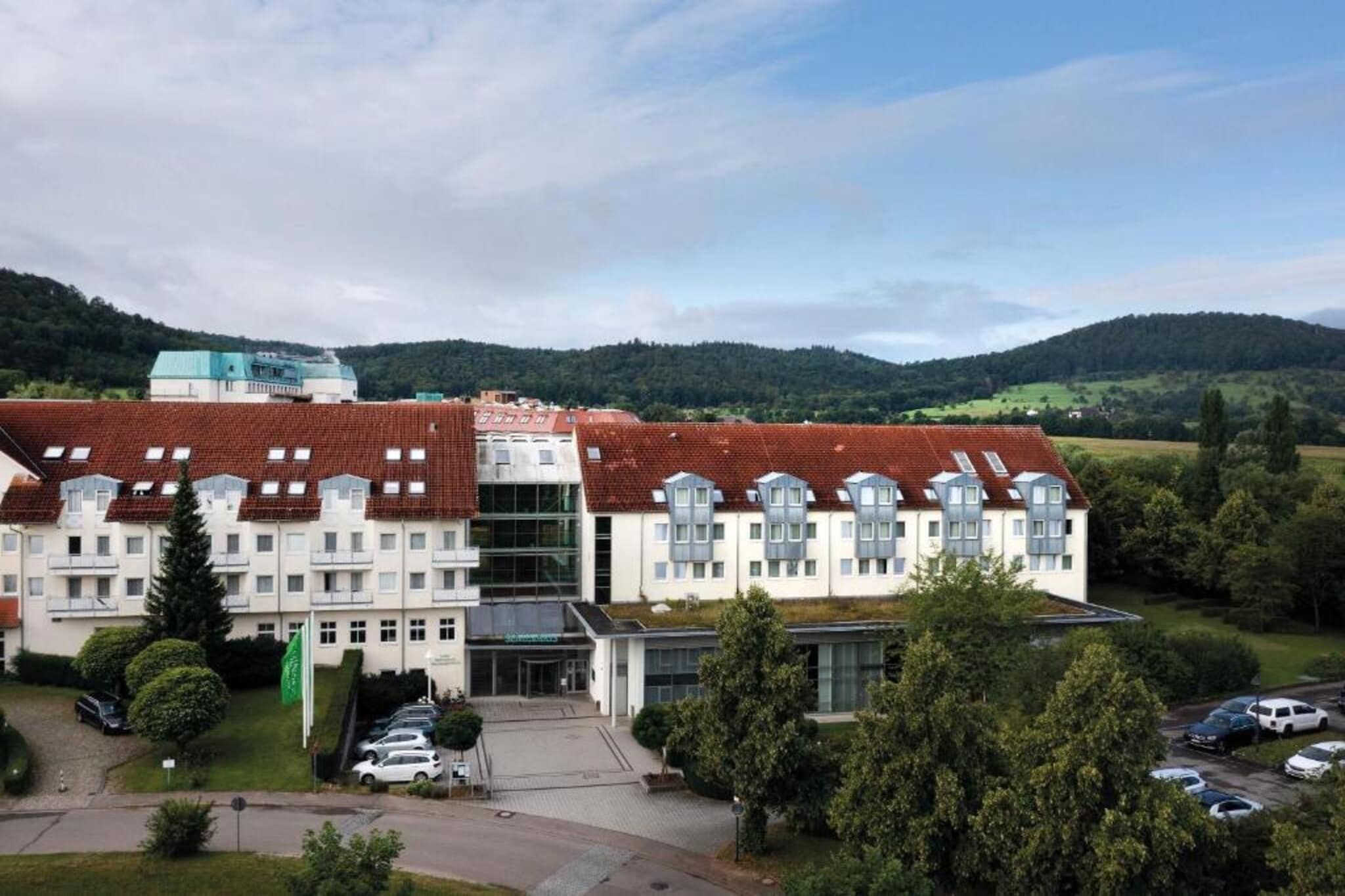Ein mehrstöckiges Hotel mit rotem Ziegeldach, einem Innenhof und Blick auf die umliegenden Hügel.