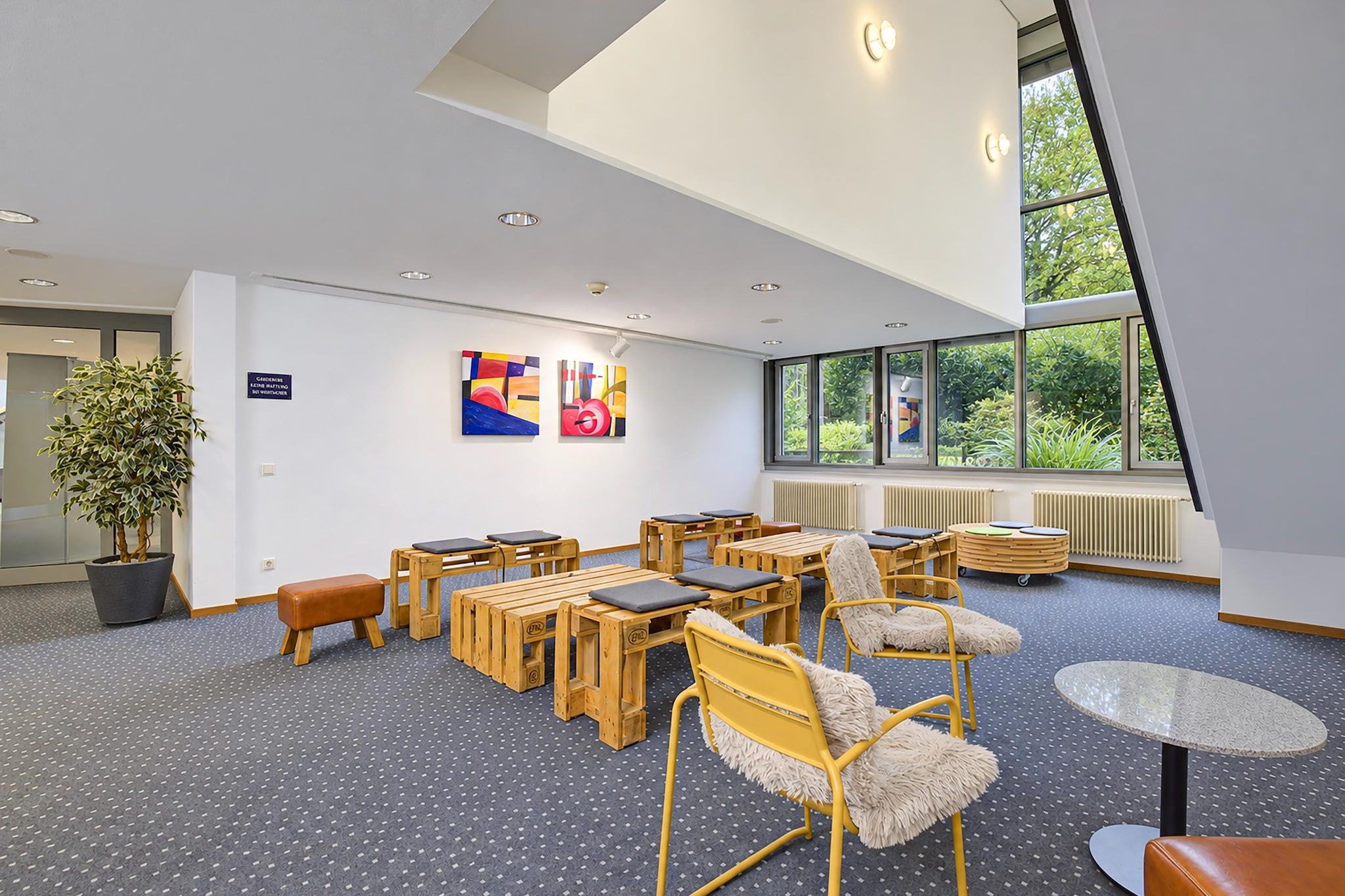 A modern interior with a high ceiling, wooden furniture, and large windows.