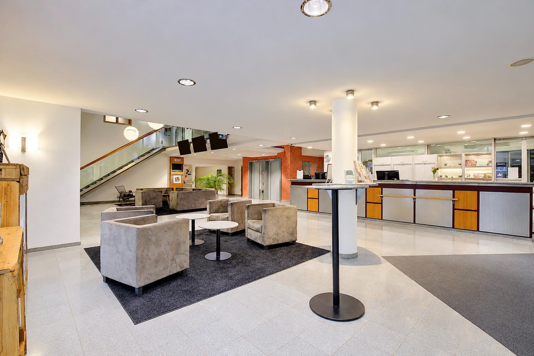 En moderne lobby med siddeområder, en receptionsdisk og en trappe.