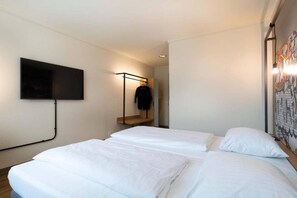 A hotel room with two beds, a TV mounted on the wall, and a coat rack with a jacket.