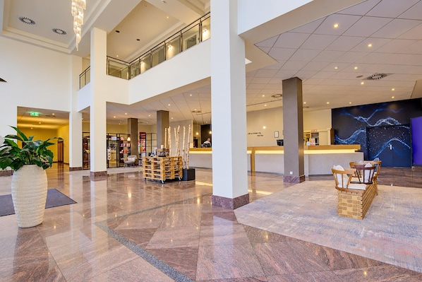 A spacious lobby with a high ceiling, a reception desk, and a seating area with chairs.