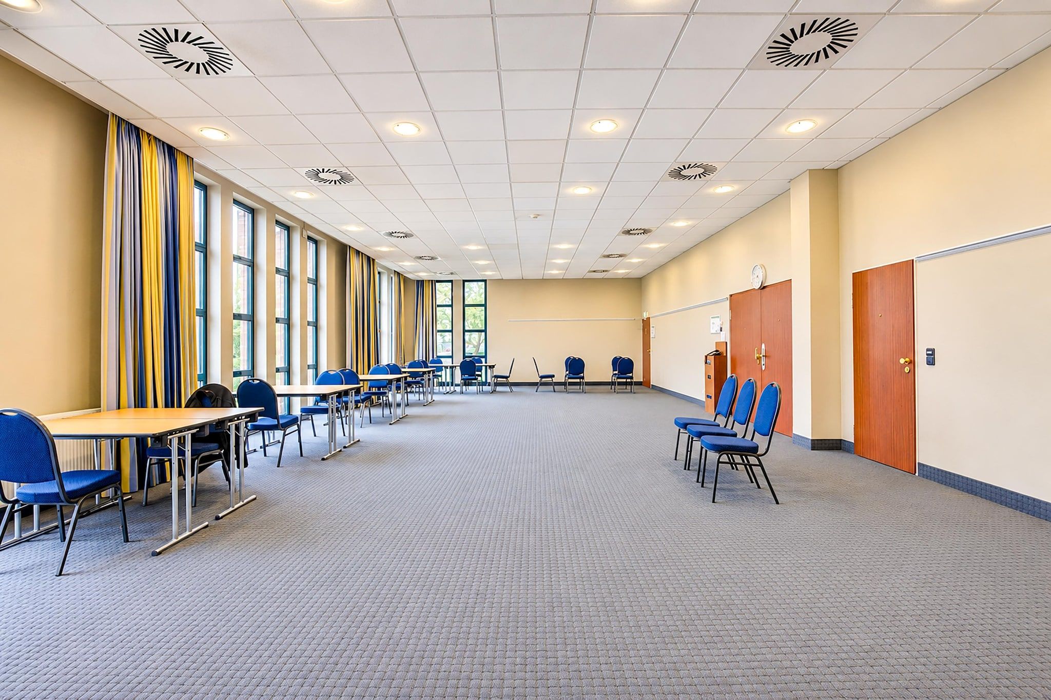 Ein Konferenzraum mit Tischen, Stühlen, großen Fenstern und Teppichboden.