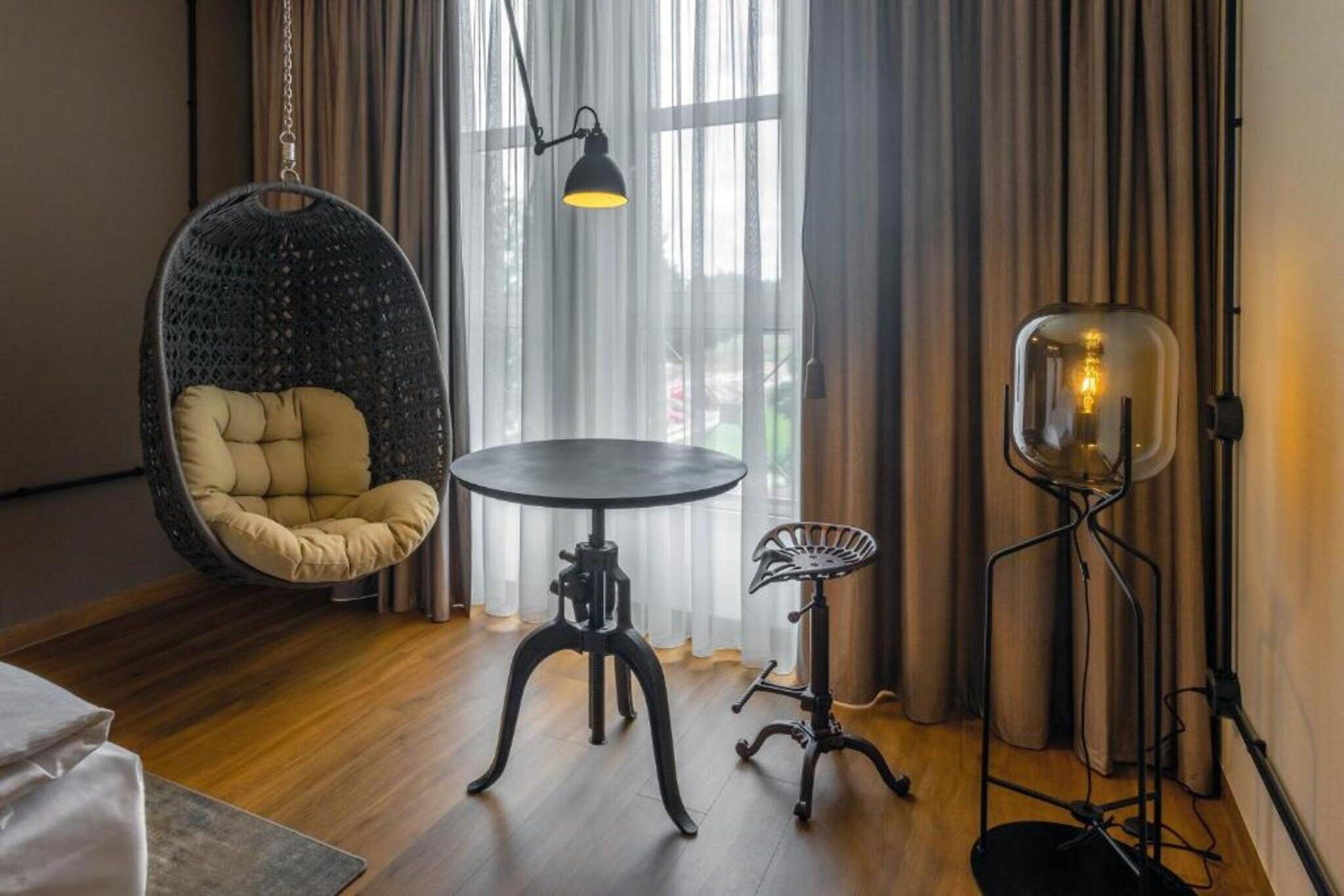 A room with a hanging chair, a round table, a floor lamp, and a small side table.
