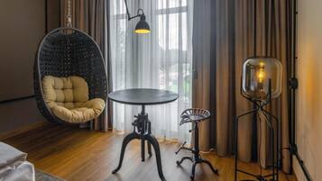 A room with a hanging chair, a round table, a floor lamp, and a small side table.
