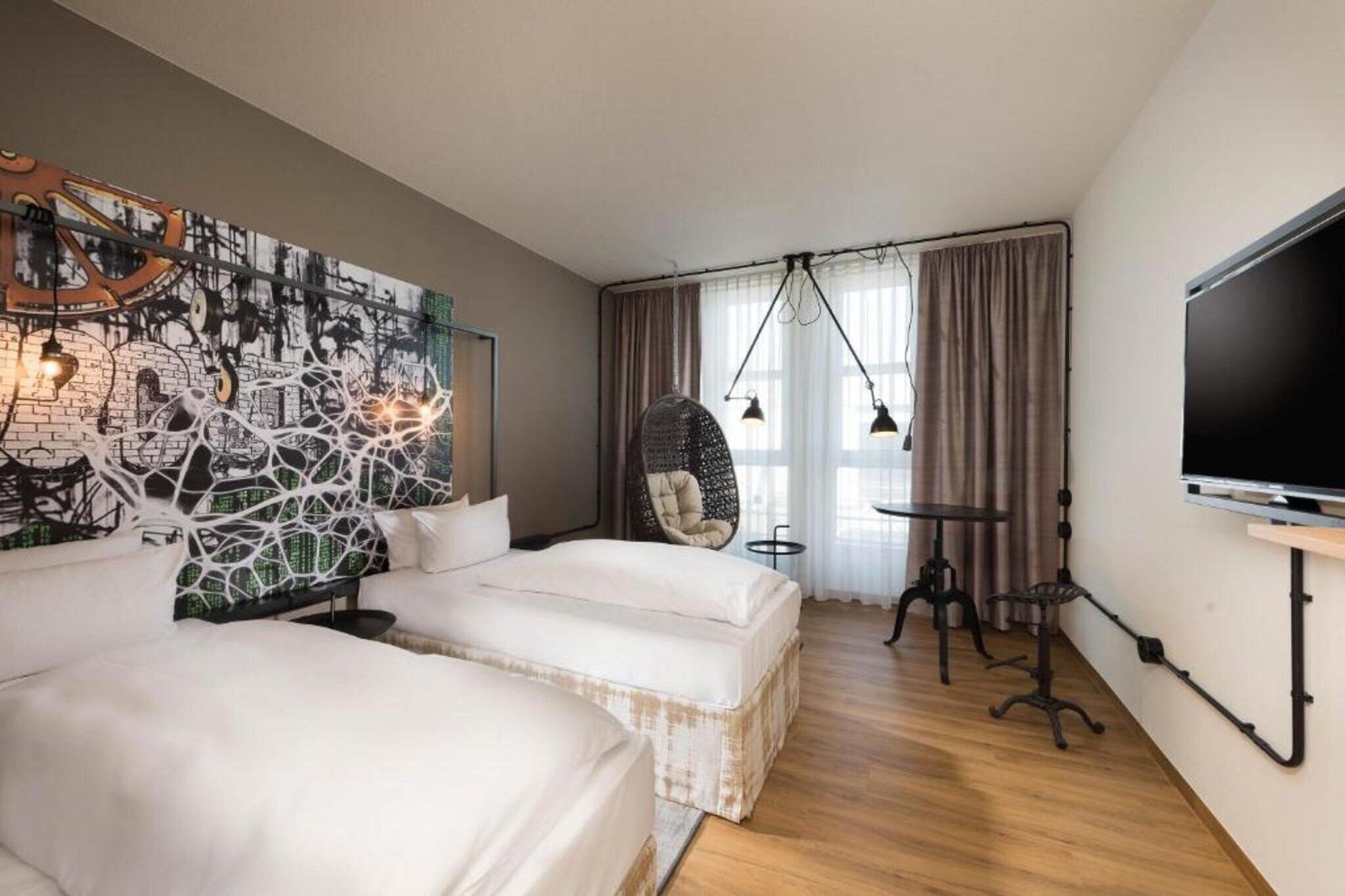 A hotel room with two beds, a hanging chair, a TV, and a wall art piece.