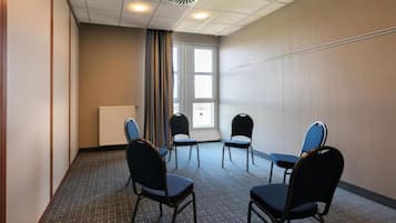 Ein Konferenzraum mit weißer Decke, einem Heizkörper und einem mit Vorhängen versehenen Fenster. Vier Stühle sind um einen Tisch angeordnet.