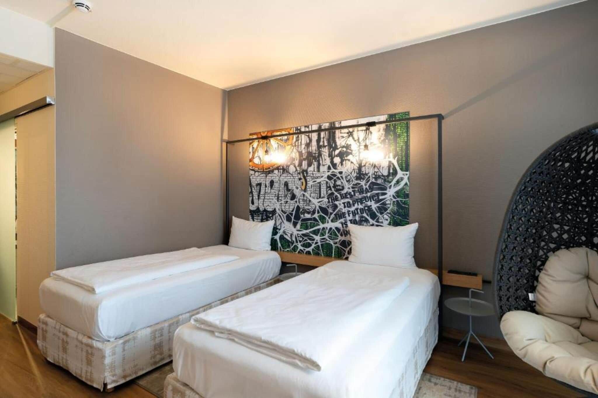 A hotel room with two beds, a large abstract painting on the wall, a chair, and a small table.