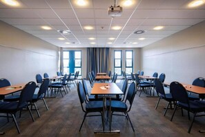 A conference room with multiple tables and chairs, large windows, and ceiling projectors.