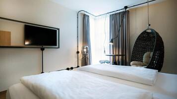 A hotel room with a bed, a television, a hanging chair, and a window with curtains.