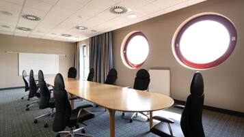 A conference room with a long table, multiple chairs, a whiteboard, and two large windows with circular frames.