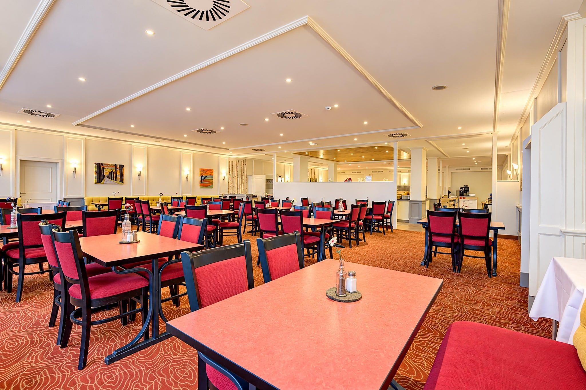 A spacious dining area with multiple tables and chairs, a central bar area, and a view of the kitchen in the background.
