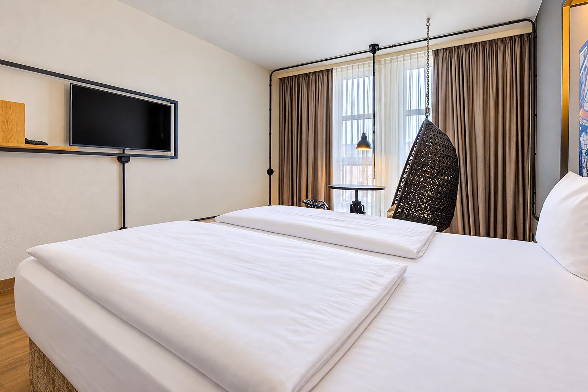 Une chambre d’hôtel avec un lit, une télévision, une fenêtre avec des rideaux et une chaise.