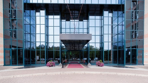 Un edificio moderno con facciata in vetro, ingresso centrale con tappeto rosso e design simmetrico.
