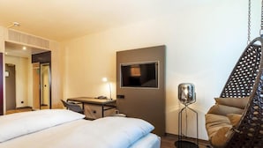 Una camera d'albergo con un letto, una scrivania, una sedia, una poltrona sospesa e un televisore montato a parete.