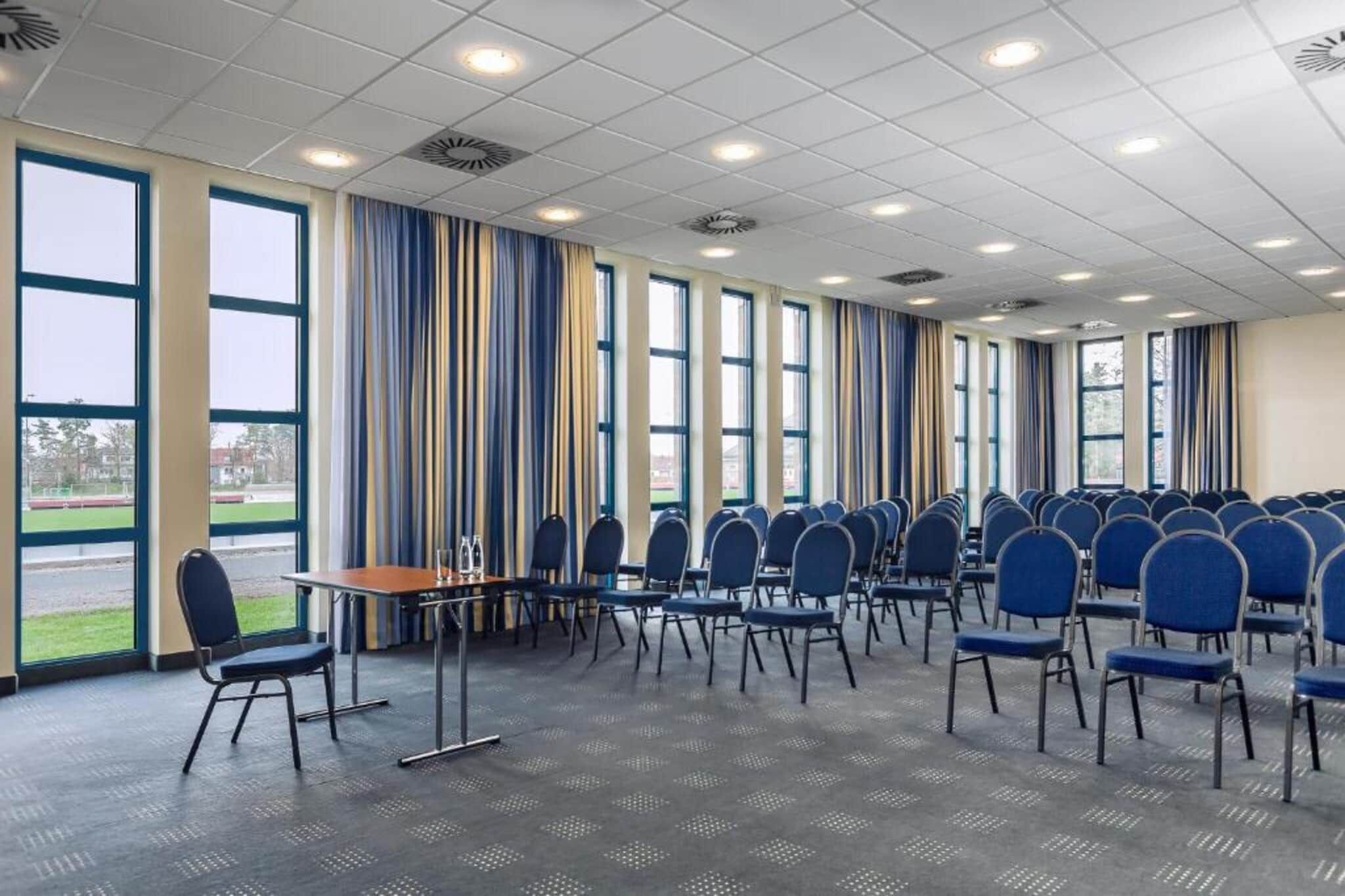 A conference room with rows of chairs, a table, and large windows.