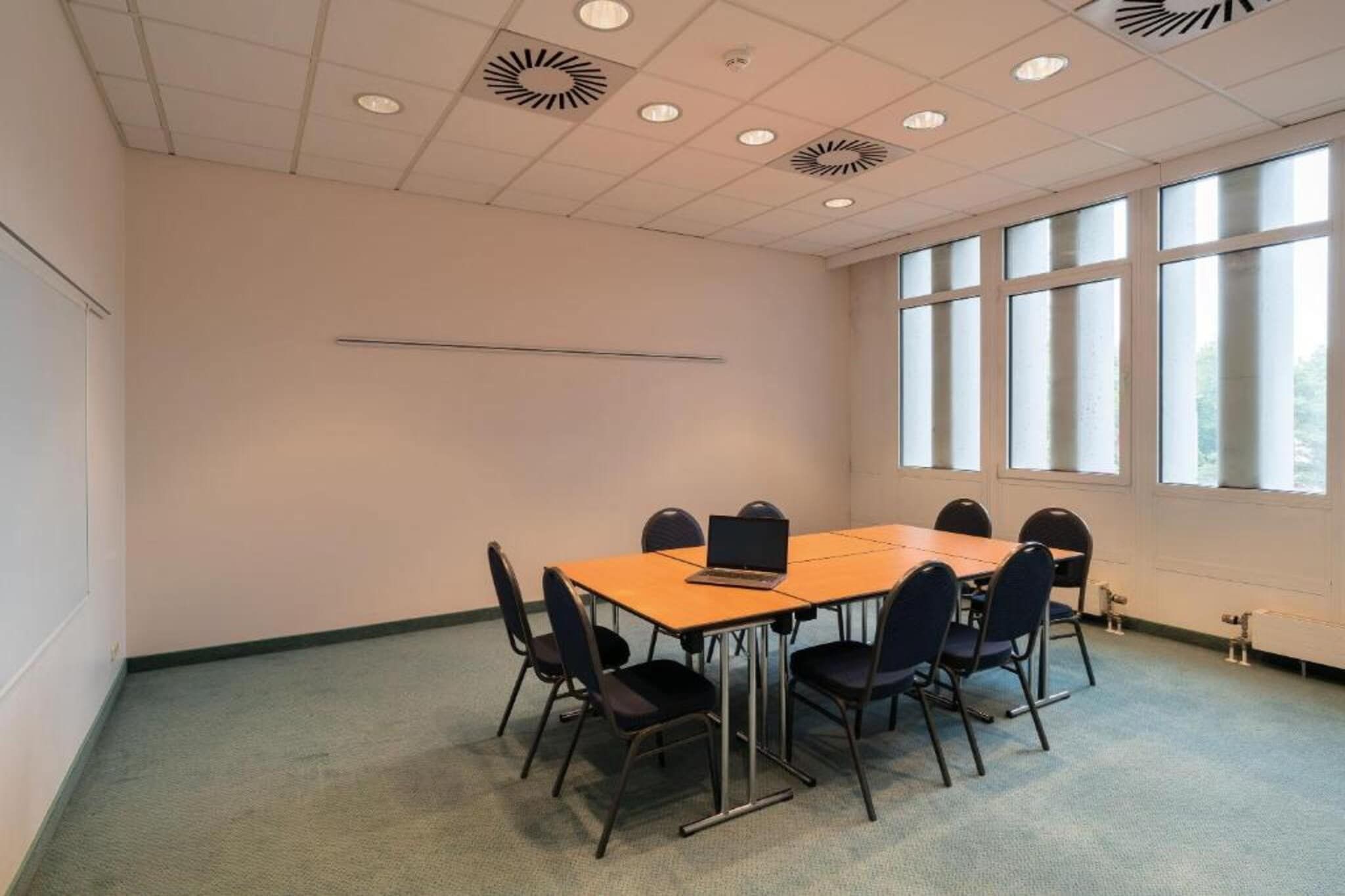 A conference room with a long table, six chairs, and a laptop on the table.
