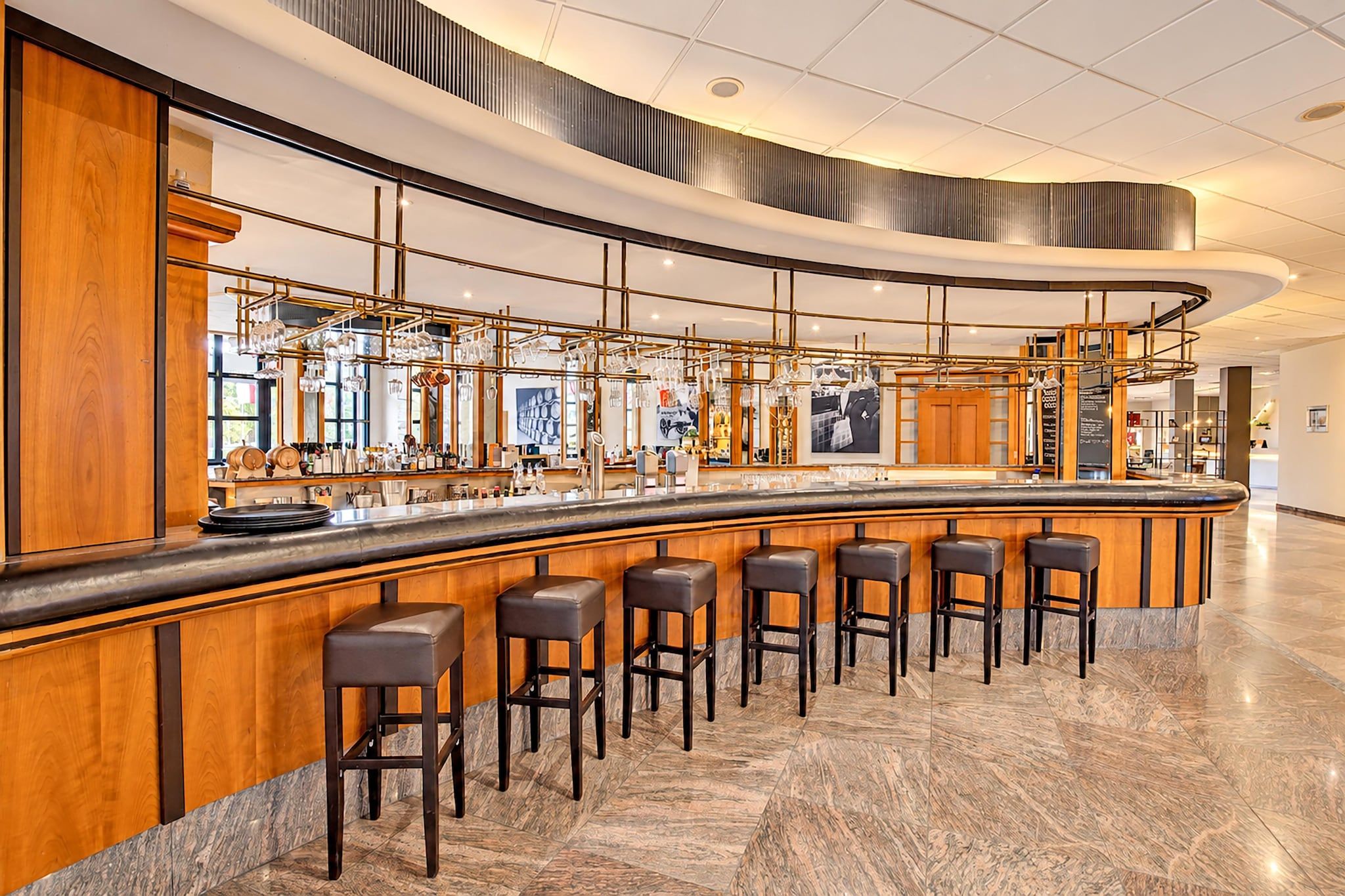 A modern bar area with a curved counter, multiple stools, and a polished marble floor.