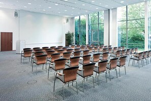 A conference room with rows of chairs, a whiteboard, and large windows with a view of greenery.