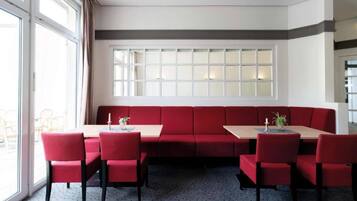 A room with a red sofa, a table, and chairs. There are windows with curtains.