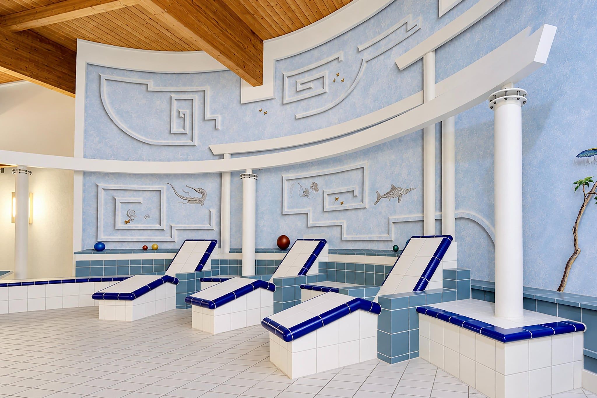 Ein Wellnessbereich mit mehreren Liegestühlen, einem Pool und dekorativen Wandbildern.