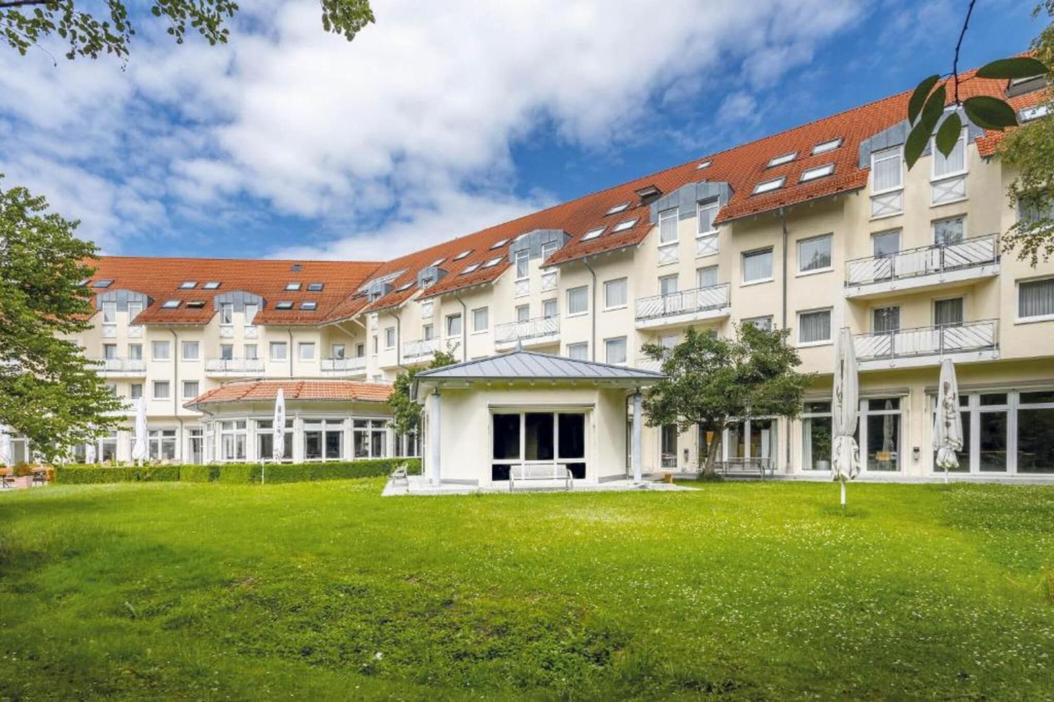 A multi-story building with a red-tiled roof, a central courtyard with a bench, and a grassy area.