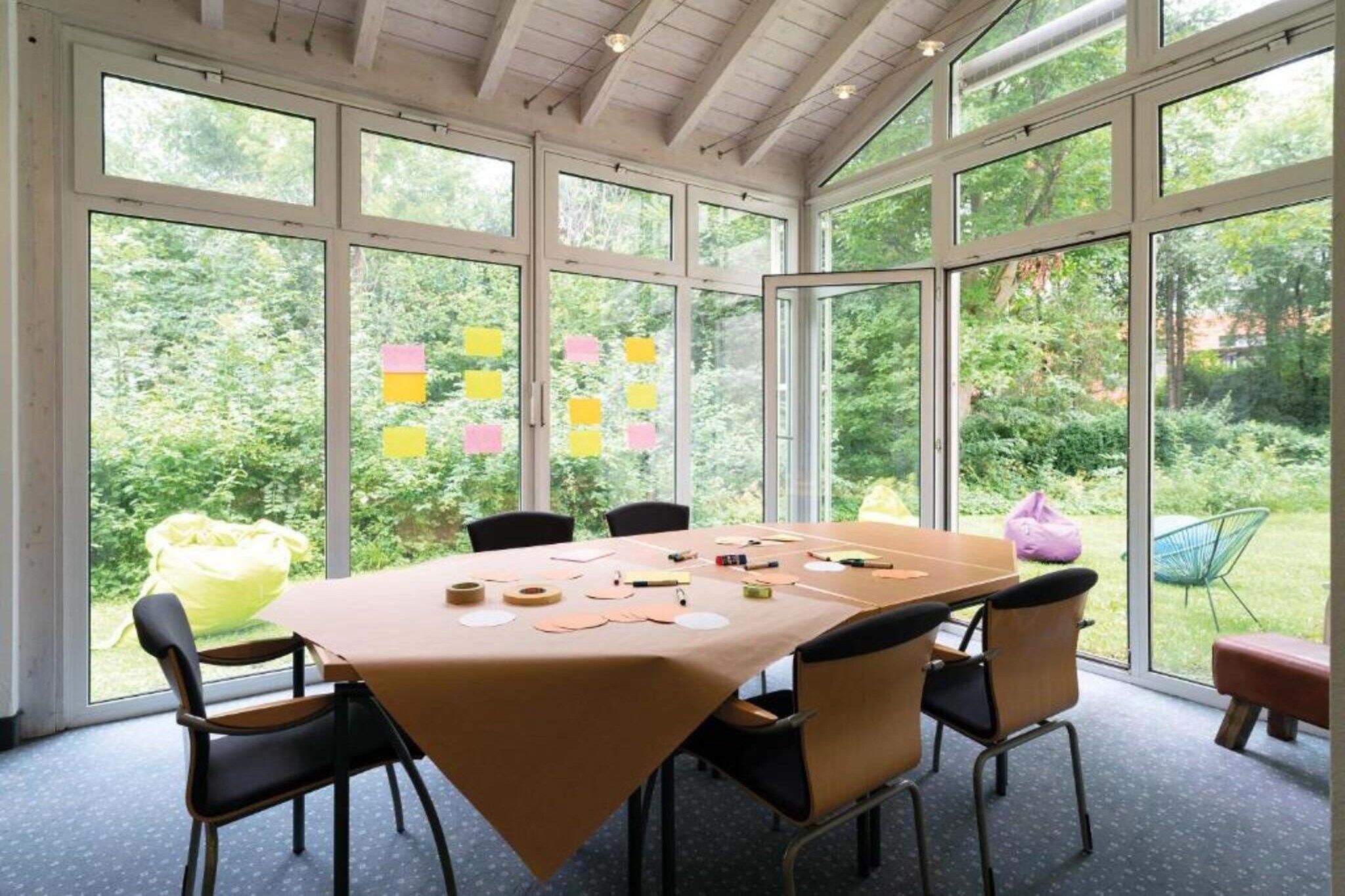Ein Konferenzraum mit großem Tisch, Stühlen und Blick auf Grün durch große Fenster.